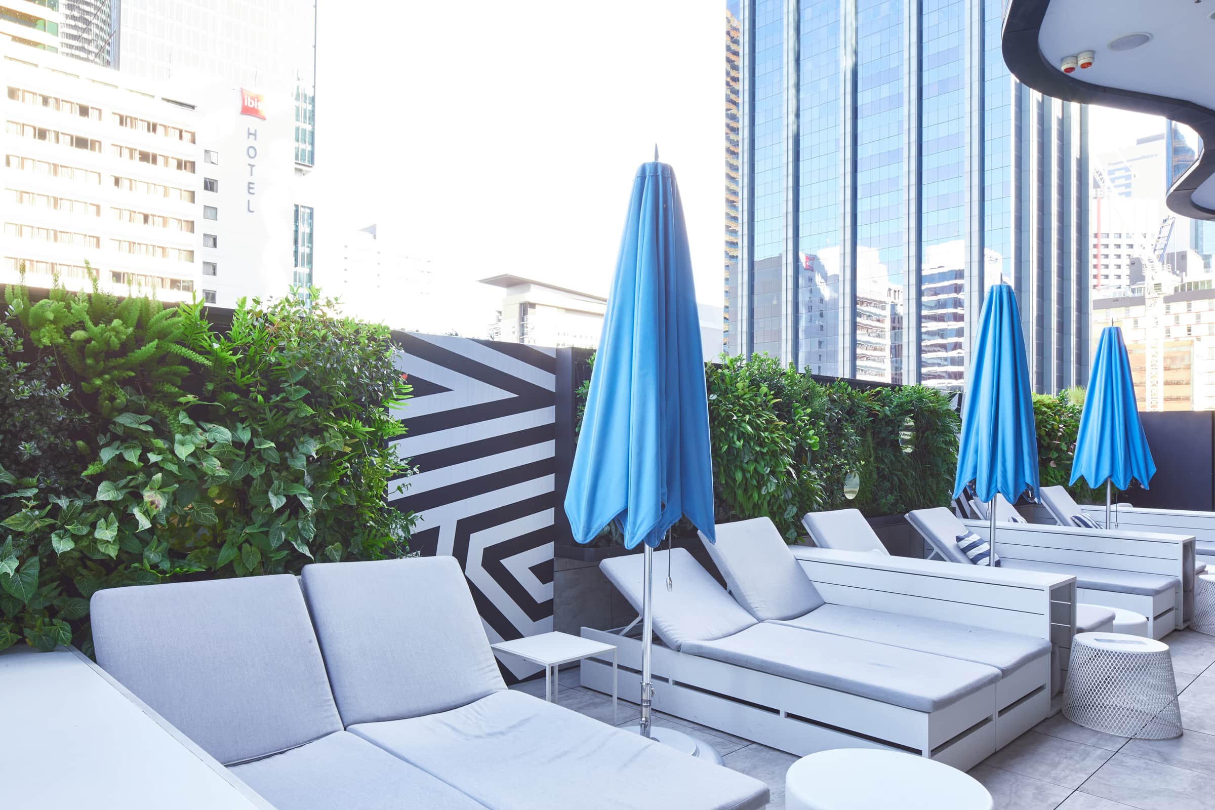 A professional photograph of W Hotel Brisbane's green walls with three closed blue umbrellas in front and pool seating.