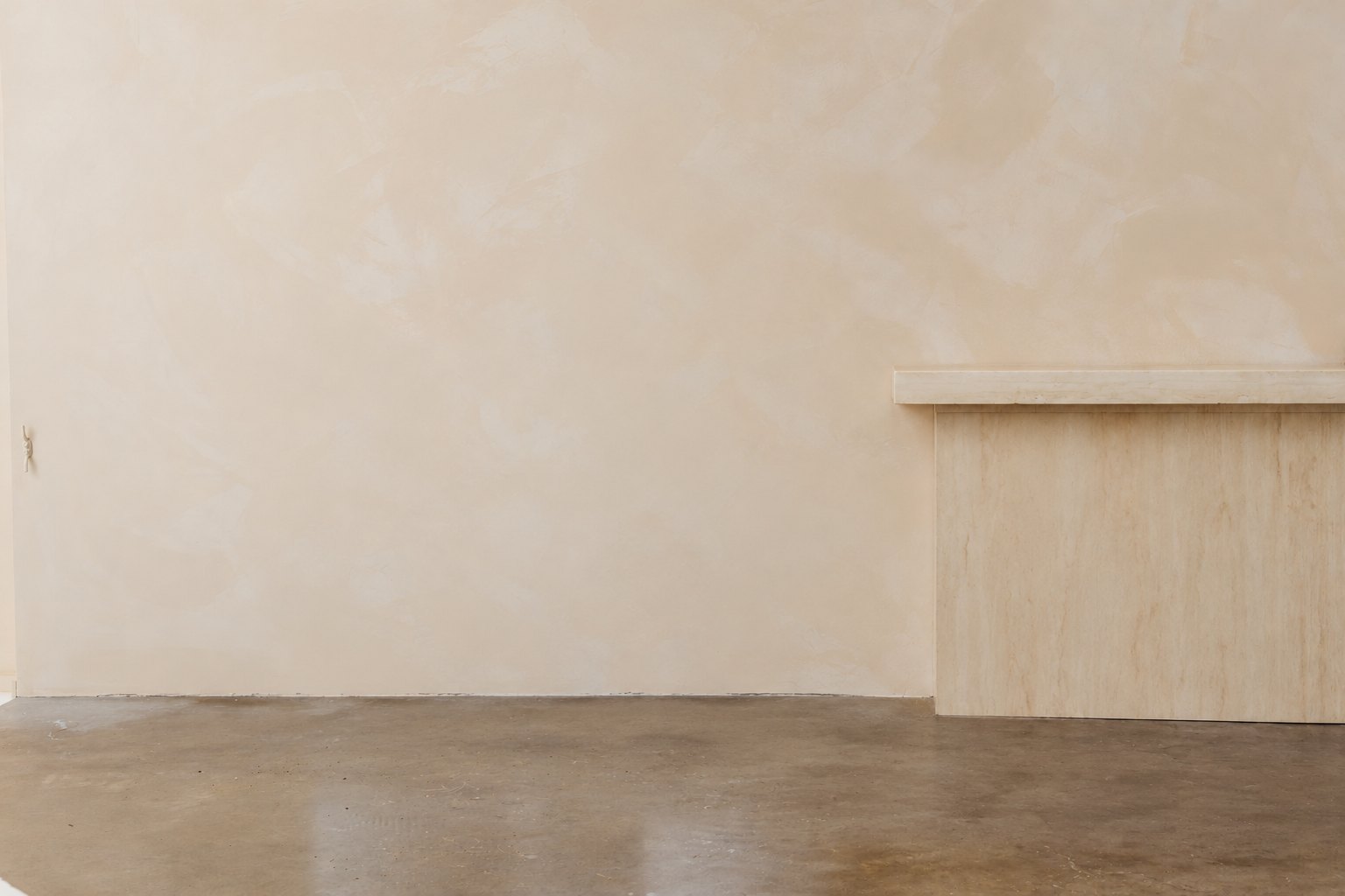 An empty event space with a bare plaster wall, polished concrete floor and travertine bench, before short-term plant hire was installed